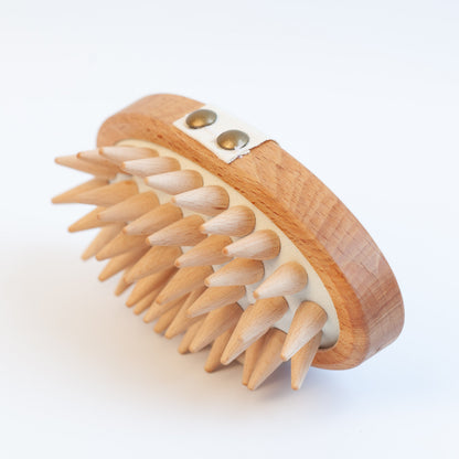 A wooden scalp massage brush with natural wood spikes and a curved wooden handle, photographed on a clean white background.