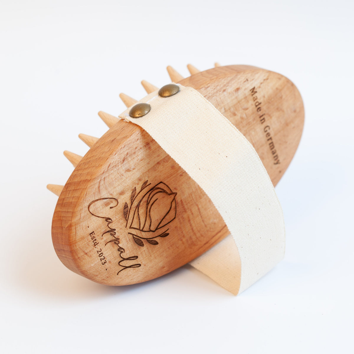 A wooden horse-shaped grooming brush with spiky teeth, a natural wood grain finish, and a white fabric strap wrapped around it. The brush is engraved with the brand name 'Cattell' and a rose logo, and features brass metal studs.