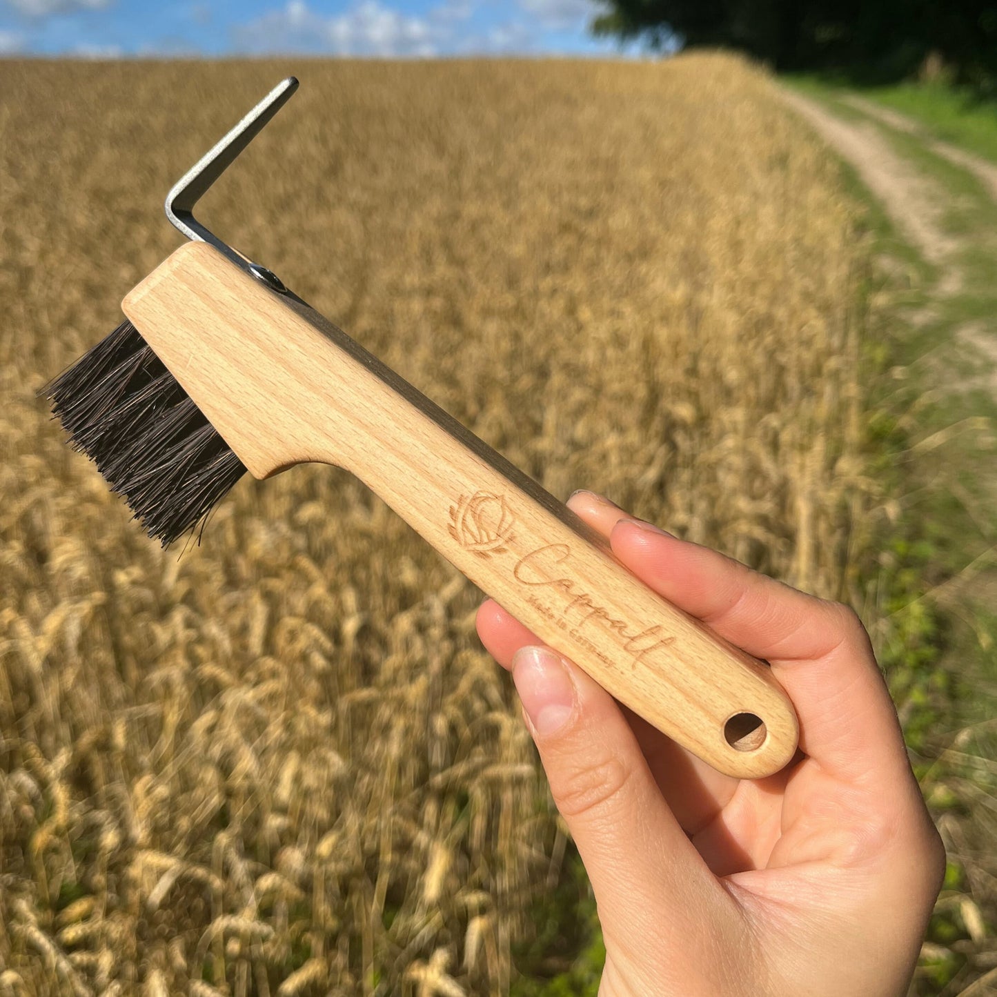 Holz Hufkratzer aus dem Pferdebürsten Set, gehalten vor grünem natürlichen Hintergrund – langlebig und effektiv.