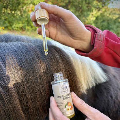 A person holding a bottle of Mane and Tail Serum and dripping the golden oil onto a horse's mane outdoors.